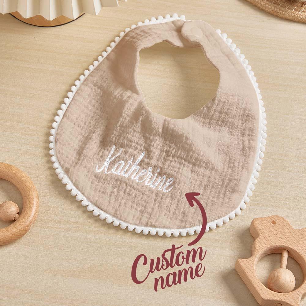Baby bib with embroidered name on a wooden surface with toys around