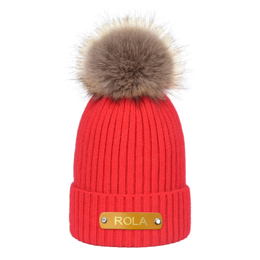 Red knit beanie with fur pom-pom and 'ROLA' label on a white background