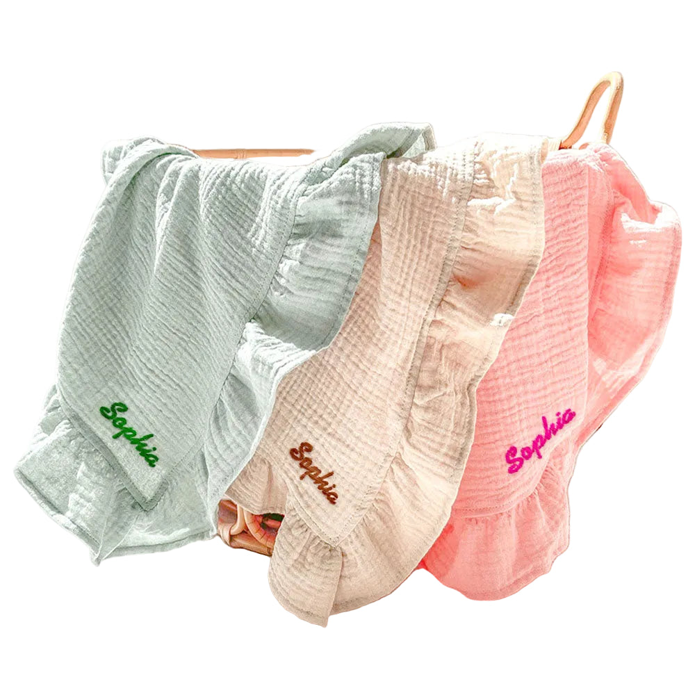 Three baby blankets in green, pink, and beige with 'Sophia' embroidered on them, hanging on a rack.