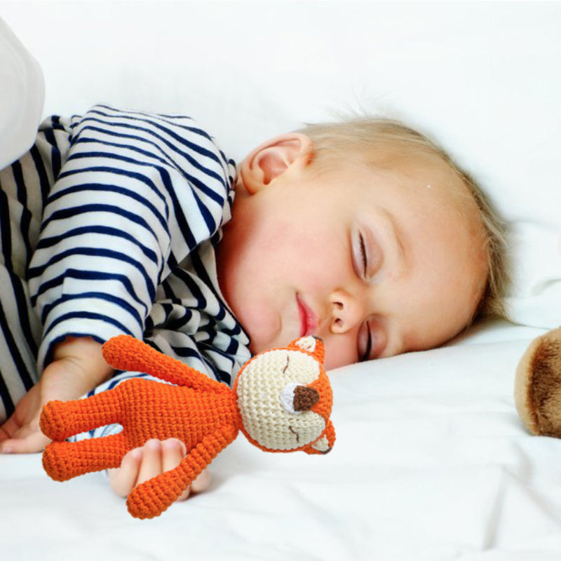Child sleeping with an orange fox toy on a white bed