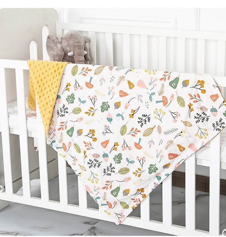 Floral-patterned baby blanket draped over a crib with a yellow blanket underneath.