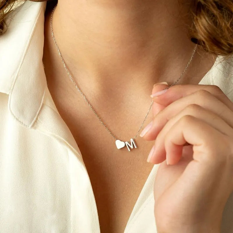 Necklace with heart and 'M' charm worn by a person