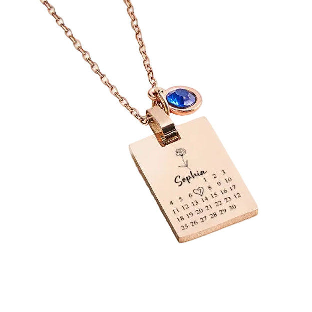 Rose gold necklace with a engraved tag and blue gemstone on a light background