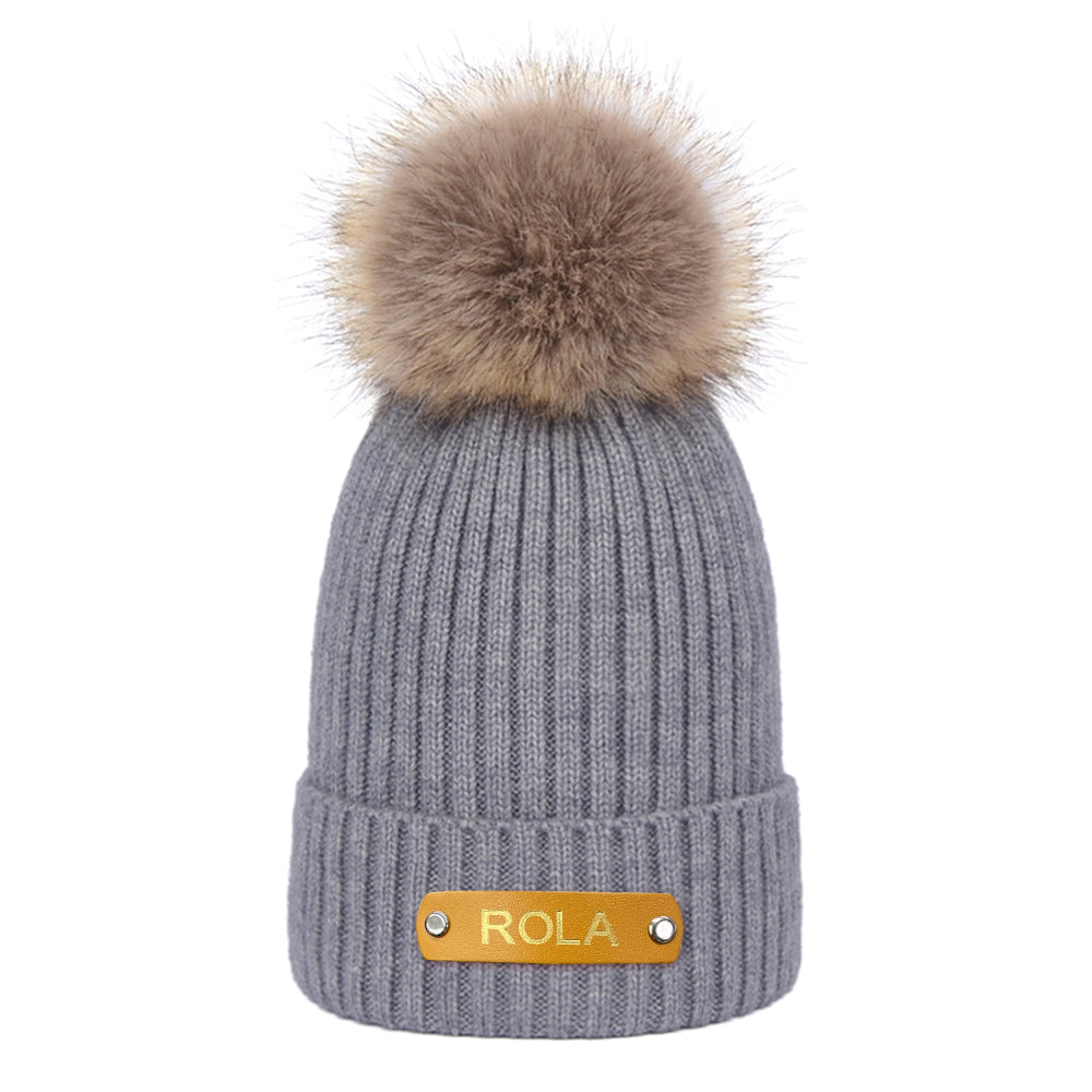 Gray knit beanie with a fur pom-pom and 'Rola' label on a white background