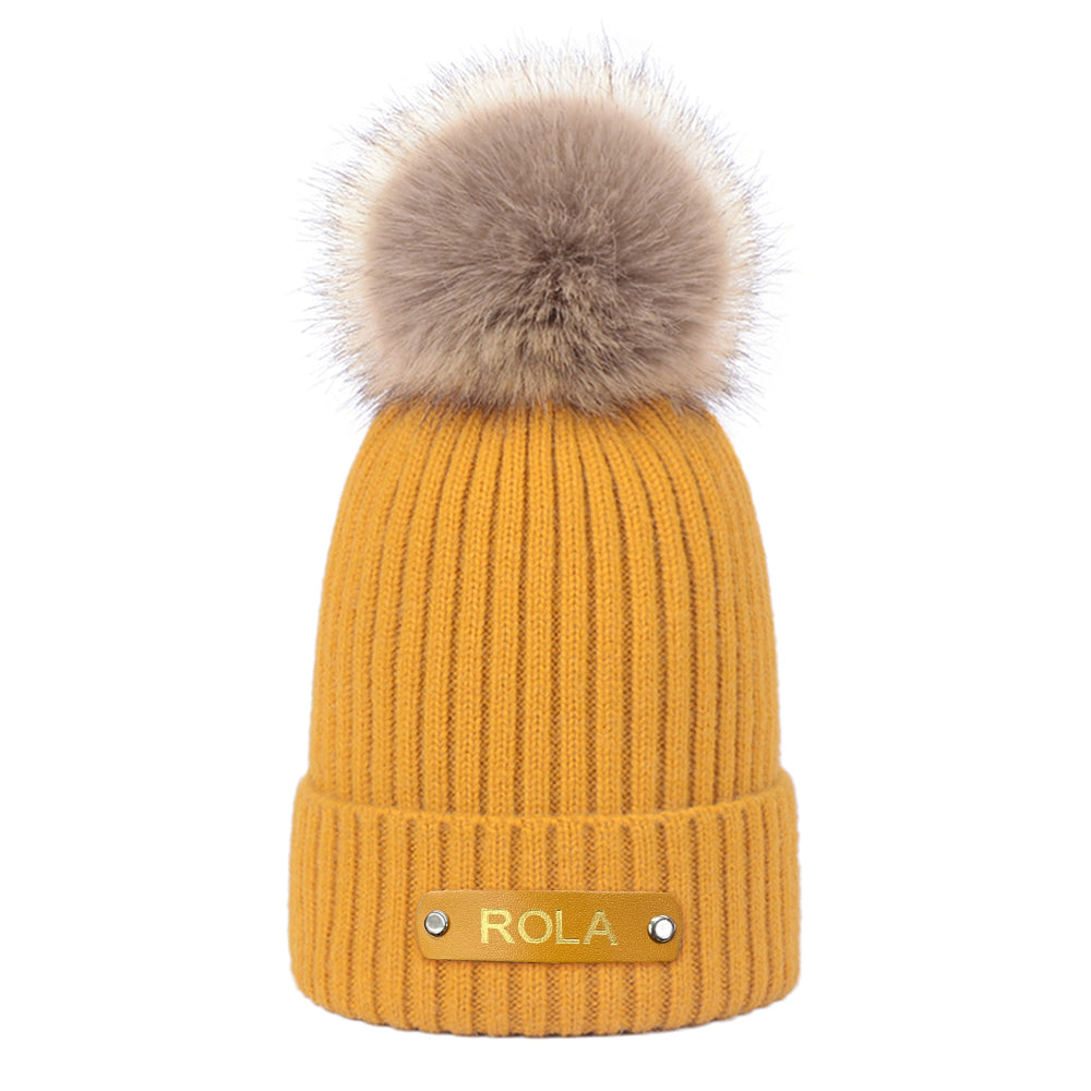 Yellow knit beanie with a fur pom-pom on a white background