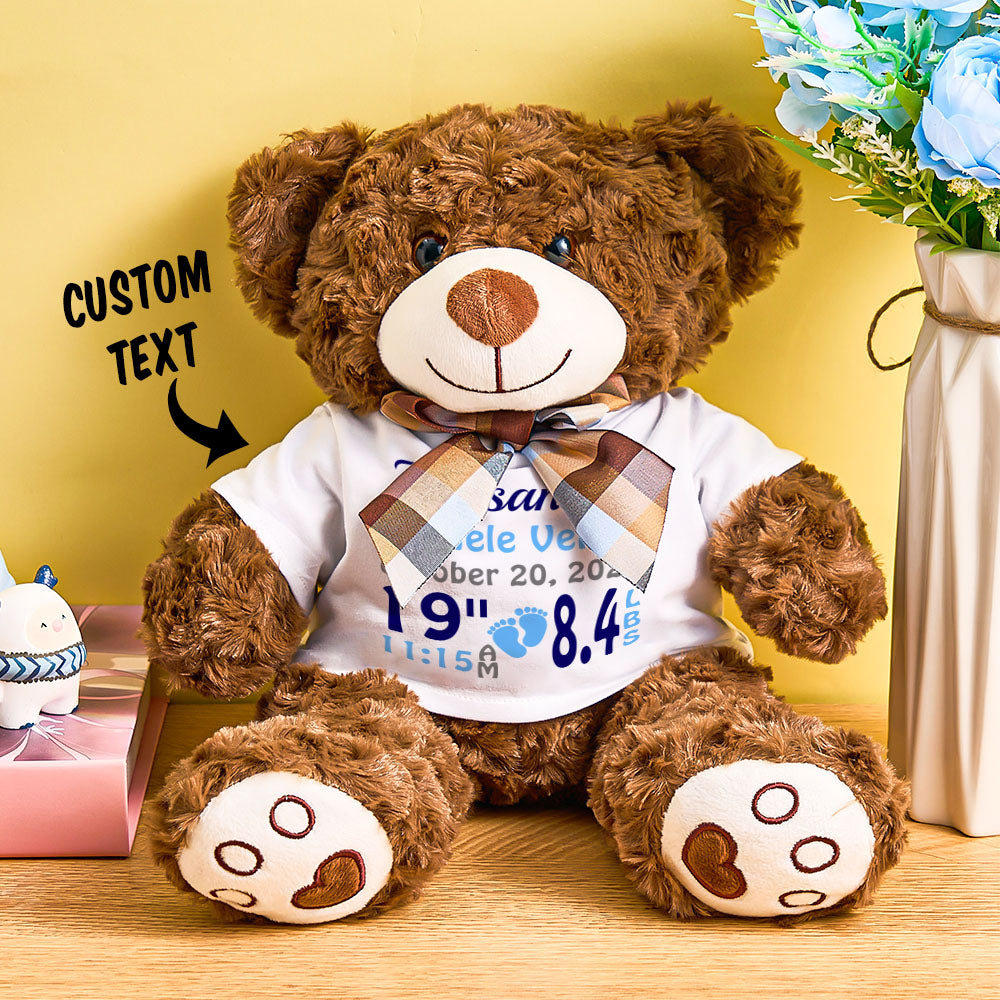 Brown teddy bear wearing a white shirt with text, sitting on a wooden surface with a yellow wall in the background.