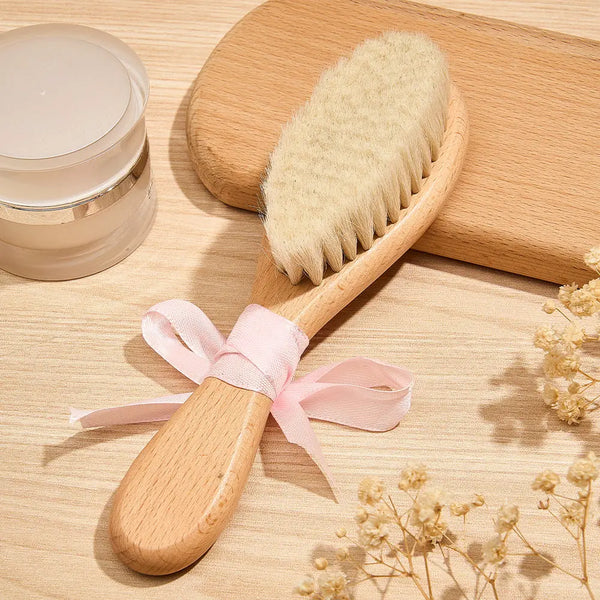 Wooden baby brush with bristles and a pink ribbon on a wooden surface with a jar and flowers.