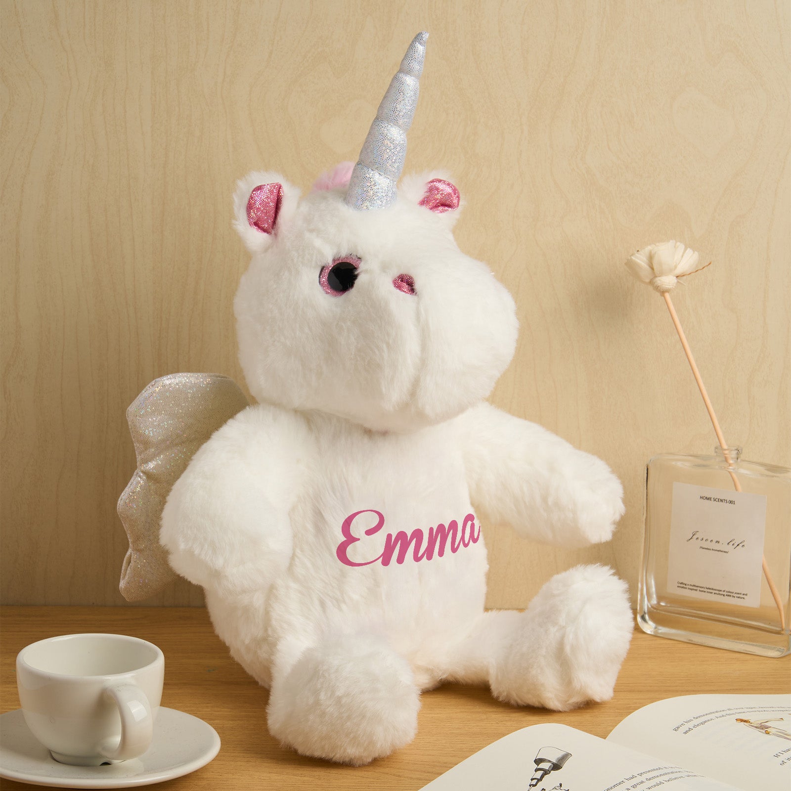 White teddy bear with unicorn horns and ears, sitting on a wooden surface with a cup and book in the background.