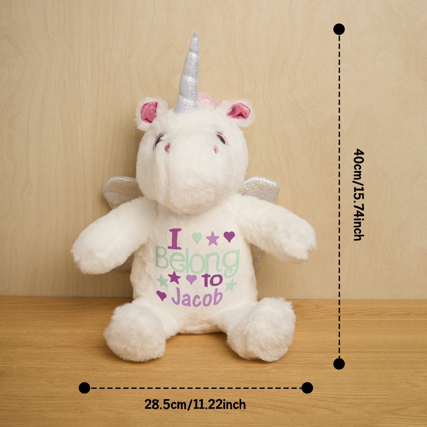Plush unicorn toy with 'I Belong to Jacob' text and measurements on a wooden surface.