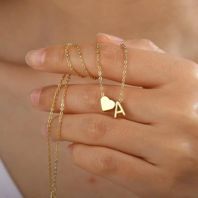 Gold necklace with a heart and 'A' pendant held by a hand