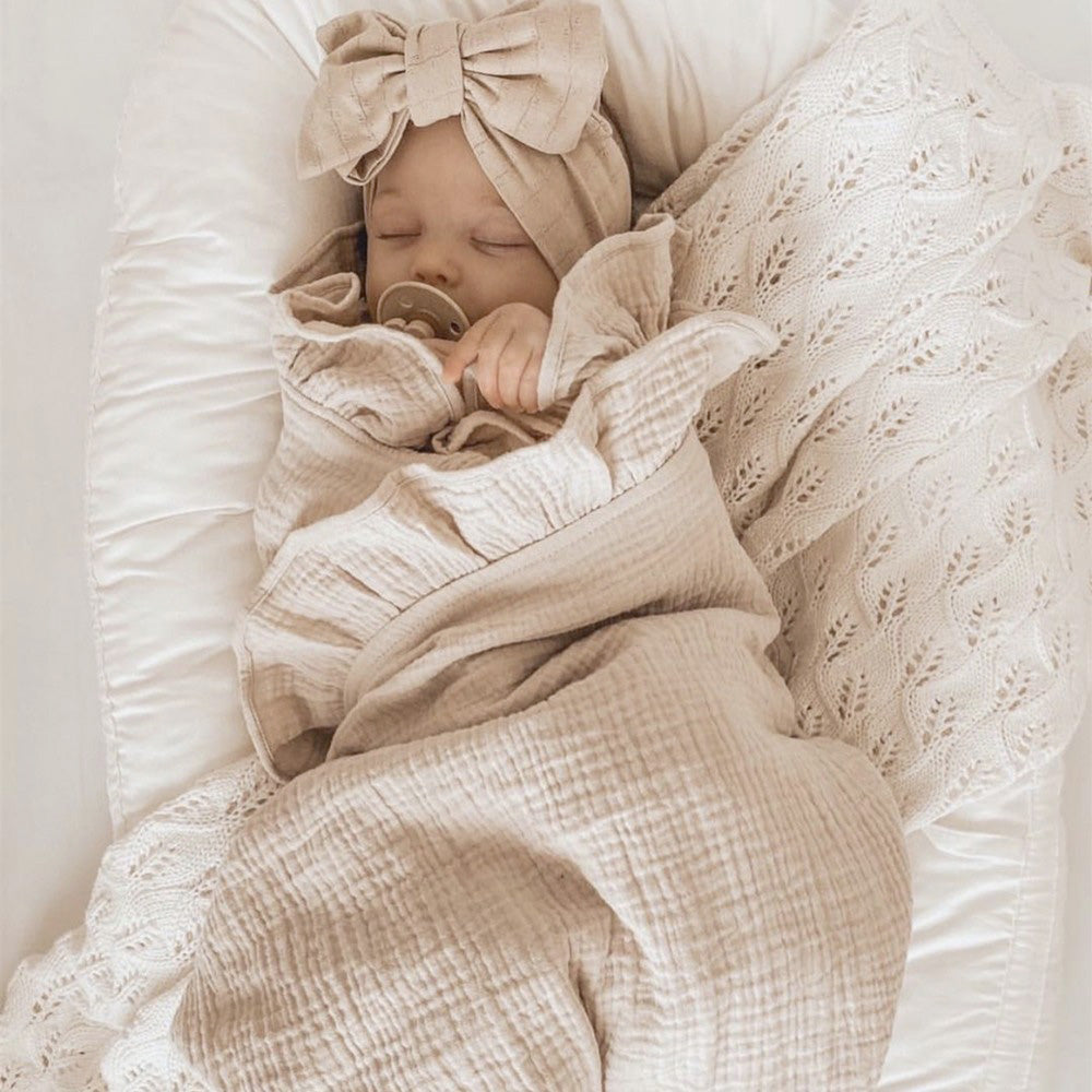 Baby wrapped in a beige blanket with a bow headband on a white background