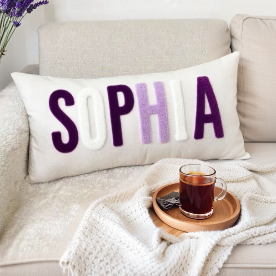 Decorative pillow with 'SOPHIA' on a couch with a cup of tea and a phone.