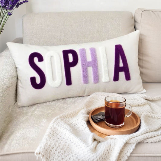 Decorative pillow with 'SOPHIA' on a couch with a cup of tea and a phone.