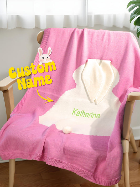 Pink blanket with a white hood and 'Katherine' printed on it, draped over a chair.