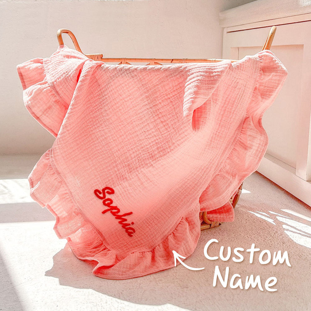 Pink ruffled blanket with 'Sophia' embroidered on it, draped over a wooden basket.