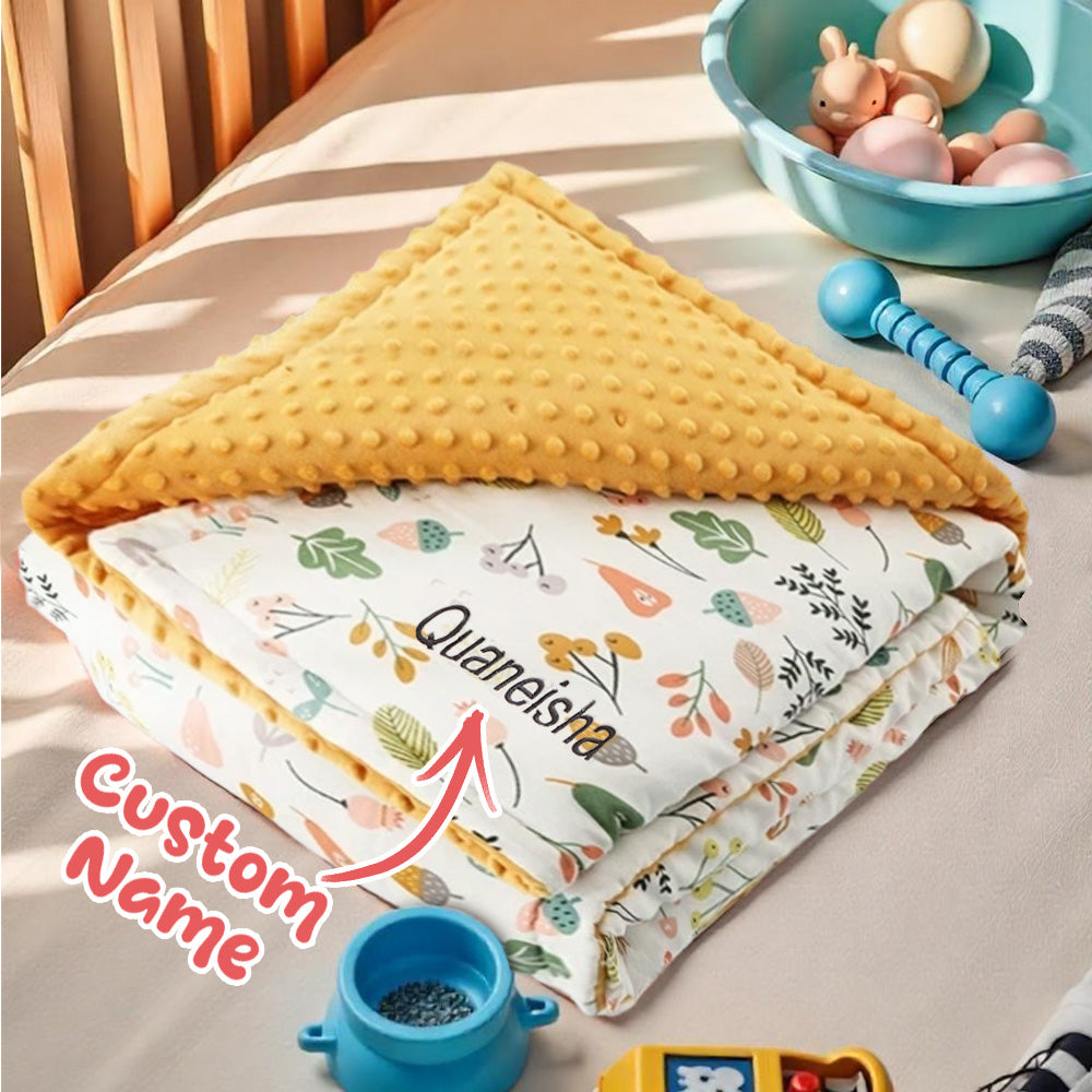 Folded blanket with floral pattern and yellow textured cover on a bed with toys in the background