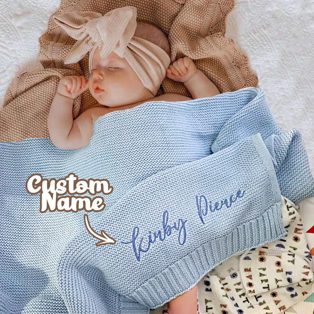 Newborn baby wrapped in a blue blanket with 'Custom Name' text, lying on a textured surface.