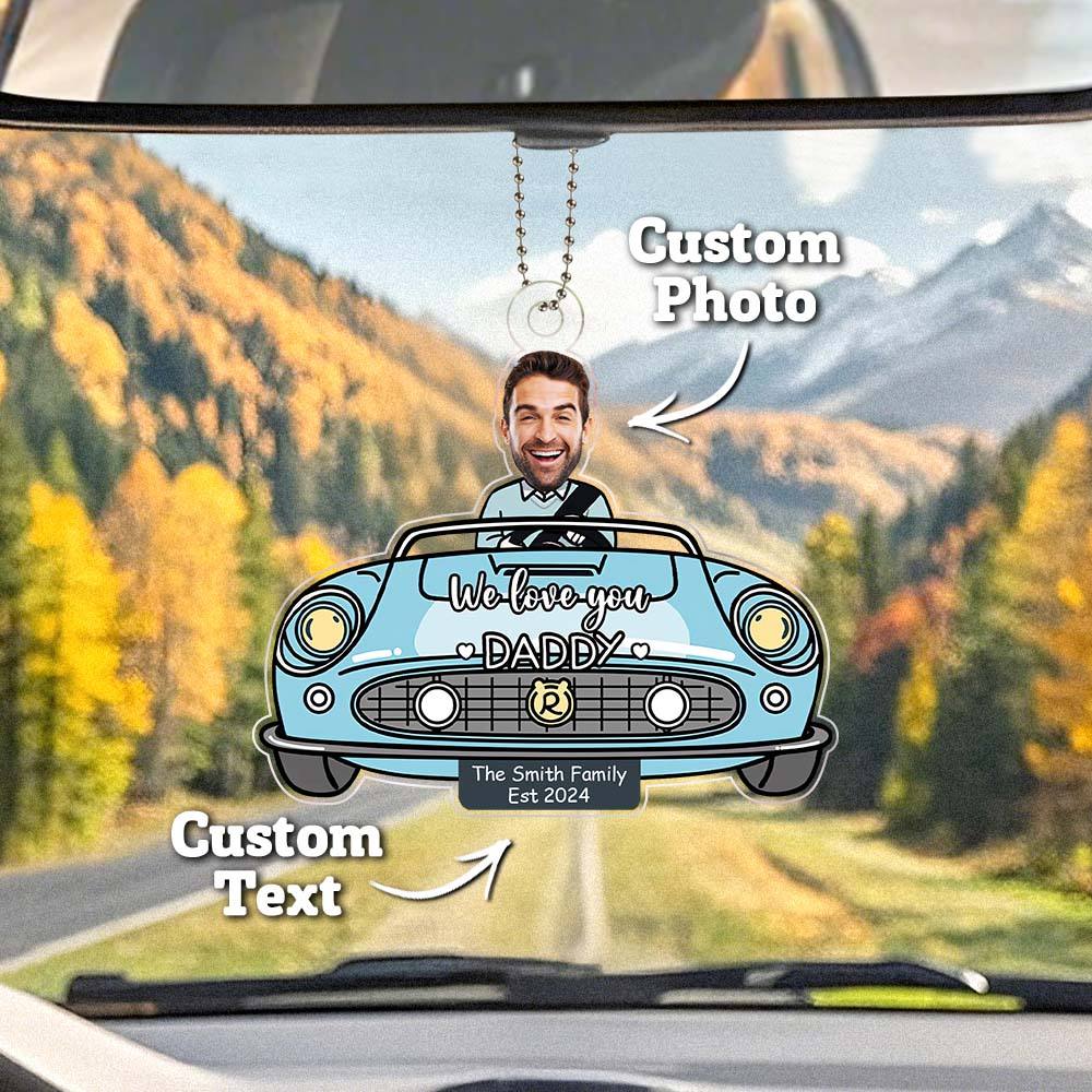 Car rearview mirror with personalized photo and text hanging from it, set against a scenic mountain backdrop.