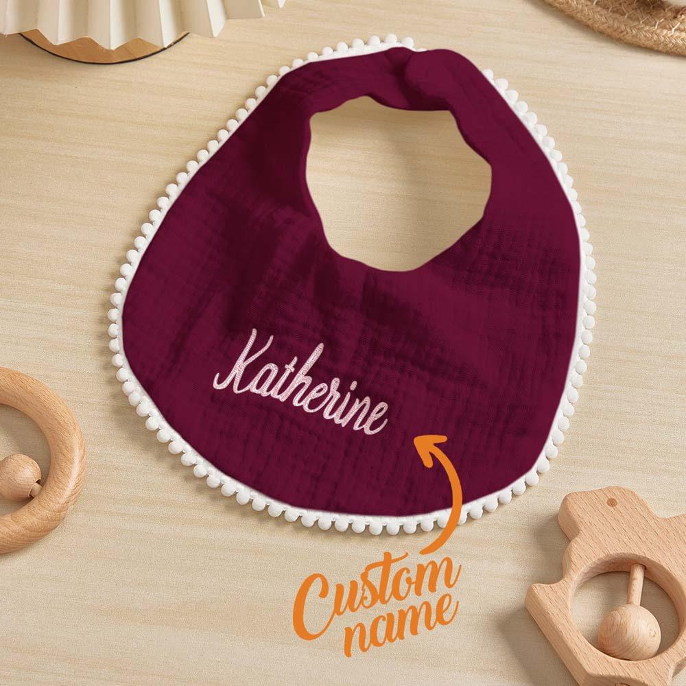 Maroon bib with 'Katherine' embroidered on it, surrounded by wooden toys on a light wood surface.