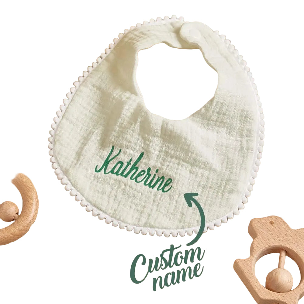White baby bib with 'Katherine' embroidered on a wooden surface with toys.