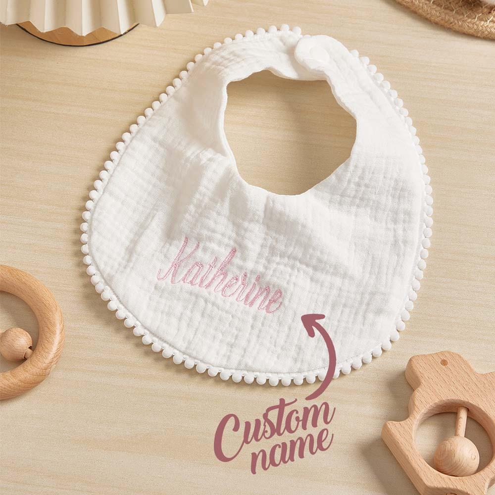 White baby bib with embroidered name on a wooden surface with wooden toys.