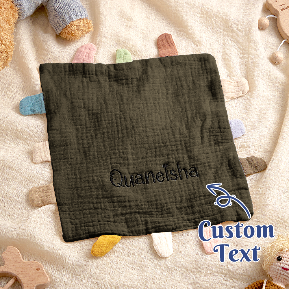 Black textured blanket with embroidered name 'Quaneisha' on a soft surface with toys.