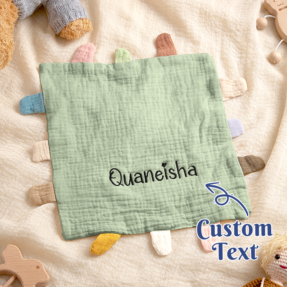 Green fabric square with embroidered name 'Quaneisha' on a soft surface with toys.