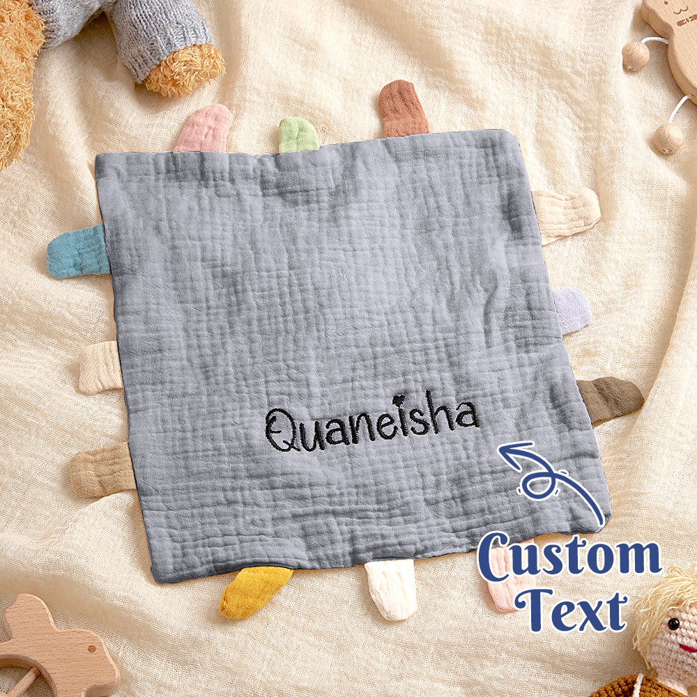 Gray baby comfort blanket with embroidered name 'Quaneisha' on a soft surface with toys.