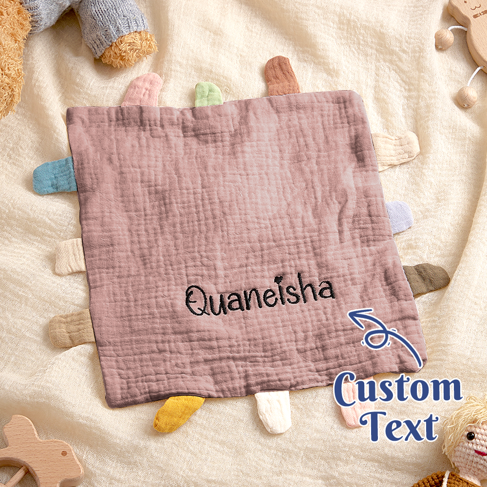 Baby comfort blanket with 'Quaneisha' text on a soft surface with toys around