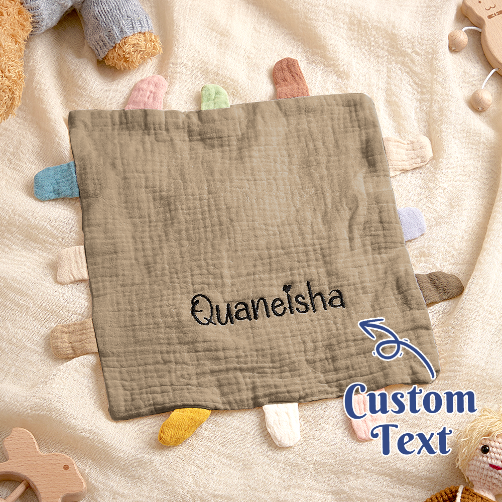 Textile product with 'Quaneisha' embroidered on it, surrounded by toys on a soft surface.
