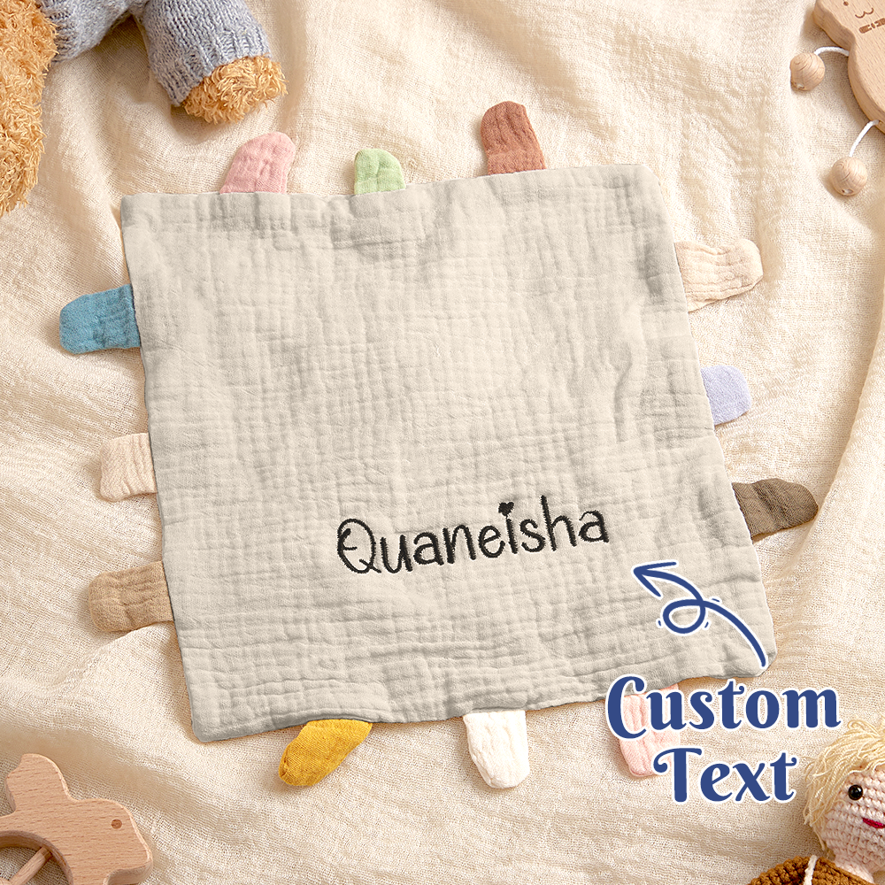 Gray soft toy with embroidered name 'Quaneisha' on a beige blanket with wooden toys.