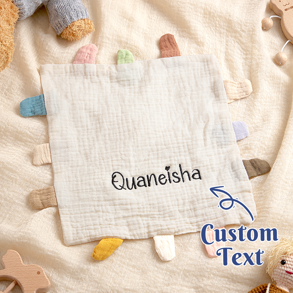 Baby comfort blanket with 'Quaneisha' text and colorful tassels on a soft surface.
