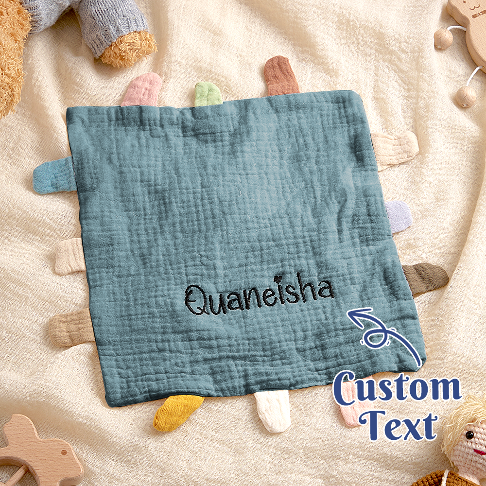 Textile product with 'Quaneisha' embroidered on it, surrounded by toys on a soft surface.
