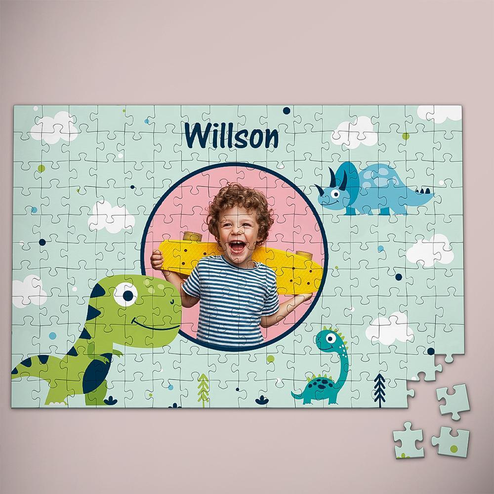 A completed personalized children's jigsaw puzzle on a light pink background. The puzzle features cartoon dinosaurs, white clouds, and the name 'Willson' at the top, with a circular cutout containing a child's photo.