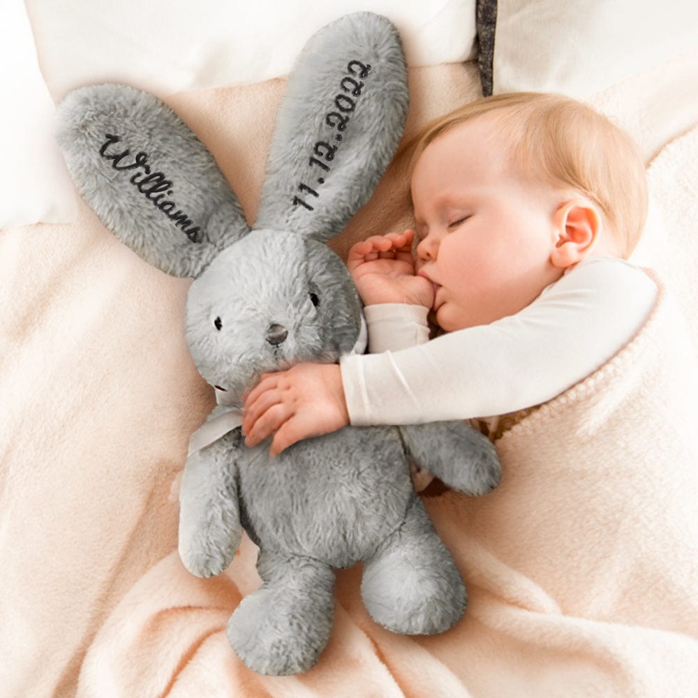 Baby sleeping with a gray plush bunny toy on a soft surface