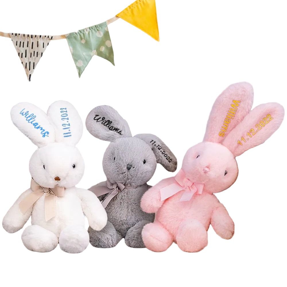 Three plush bunny toys in white, gray, and pink with personalized names on a shelf.