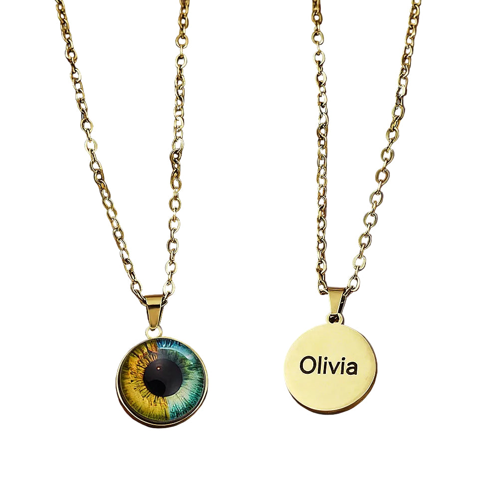 Two gold necklaces on a leather surface, one with an eye design pendant and the other with a 'Olivia' engraved pendant.