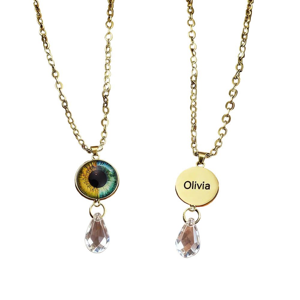 Two gold necklaces with eye-shaped and circular pendants on a brown leather surface.