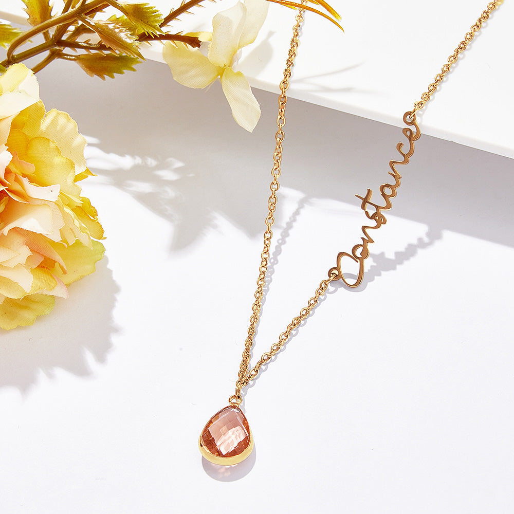 Gold necklace with a teardrop pendant on a white surface with yellow flowers.