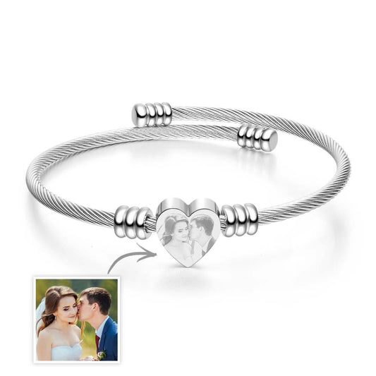 Silver bracelet with a heart-shaped charm featuring an engraved photo of a couple on a white background.