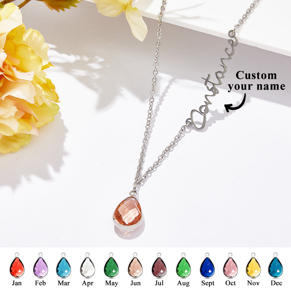 Necklace with a teardrop-shaped pendant and customizable name on a white surface with flowers.