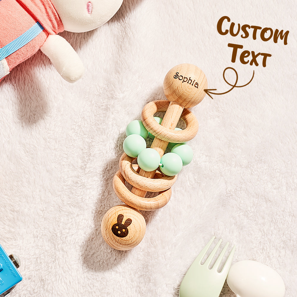 Wooden teething ring with green beads on a soft surface, featuring the name 'Sophie'.