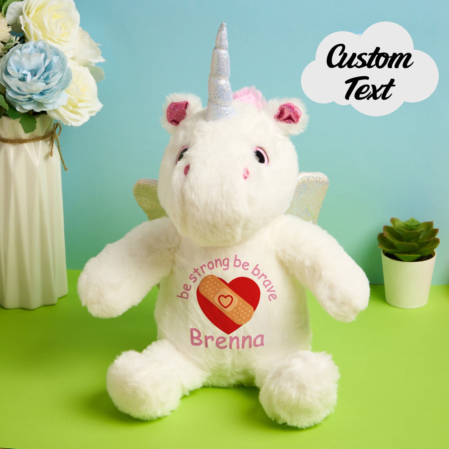 White unicorn plush toy with motivational text and a heart on a green surface with flowers and a plant in the background.