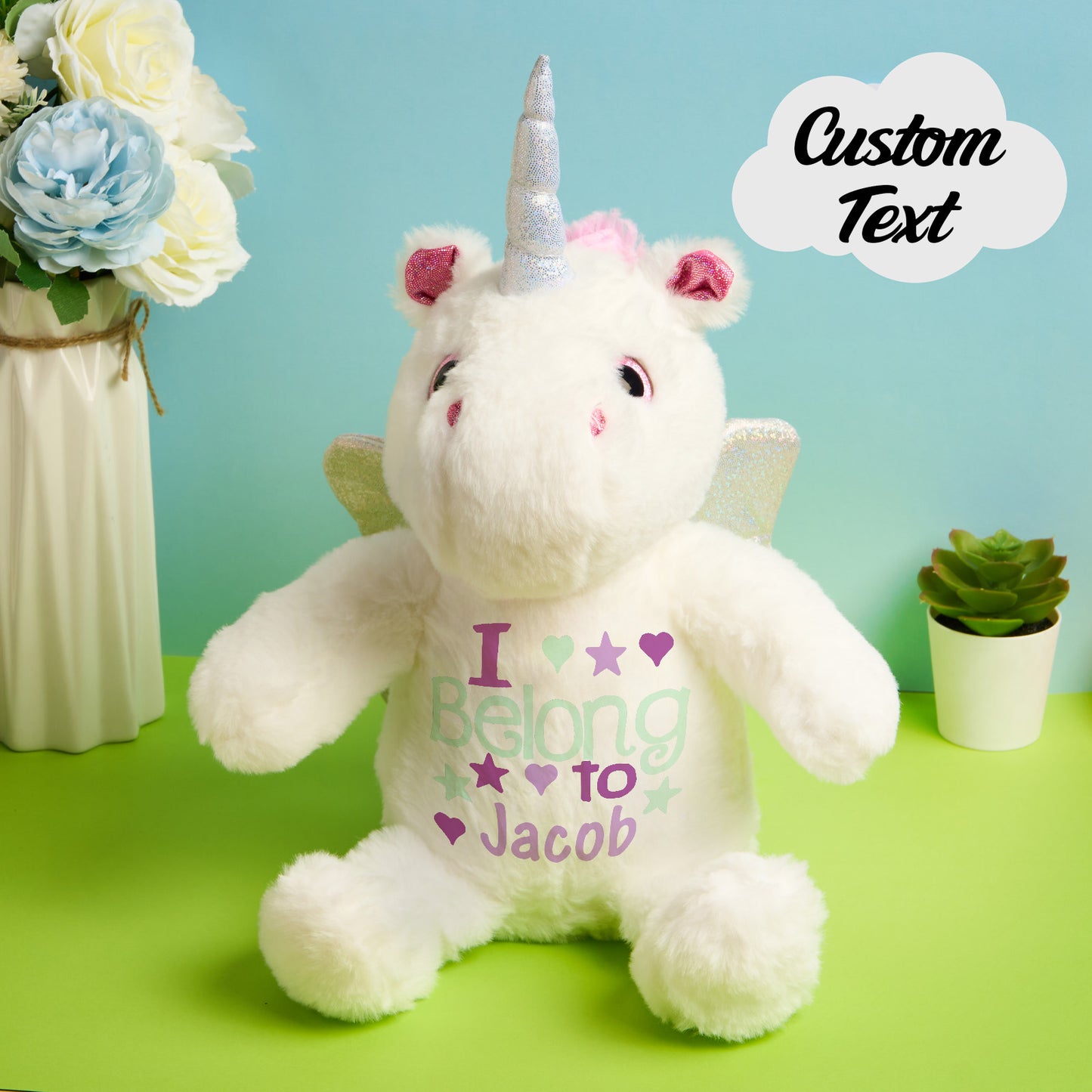White unicorn plush toy with personalized text on a green surface with decorative elements.
