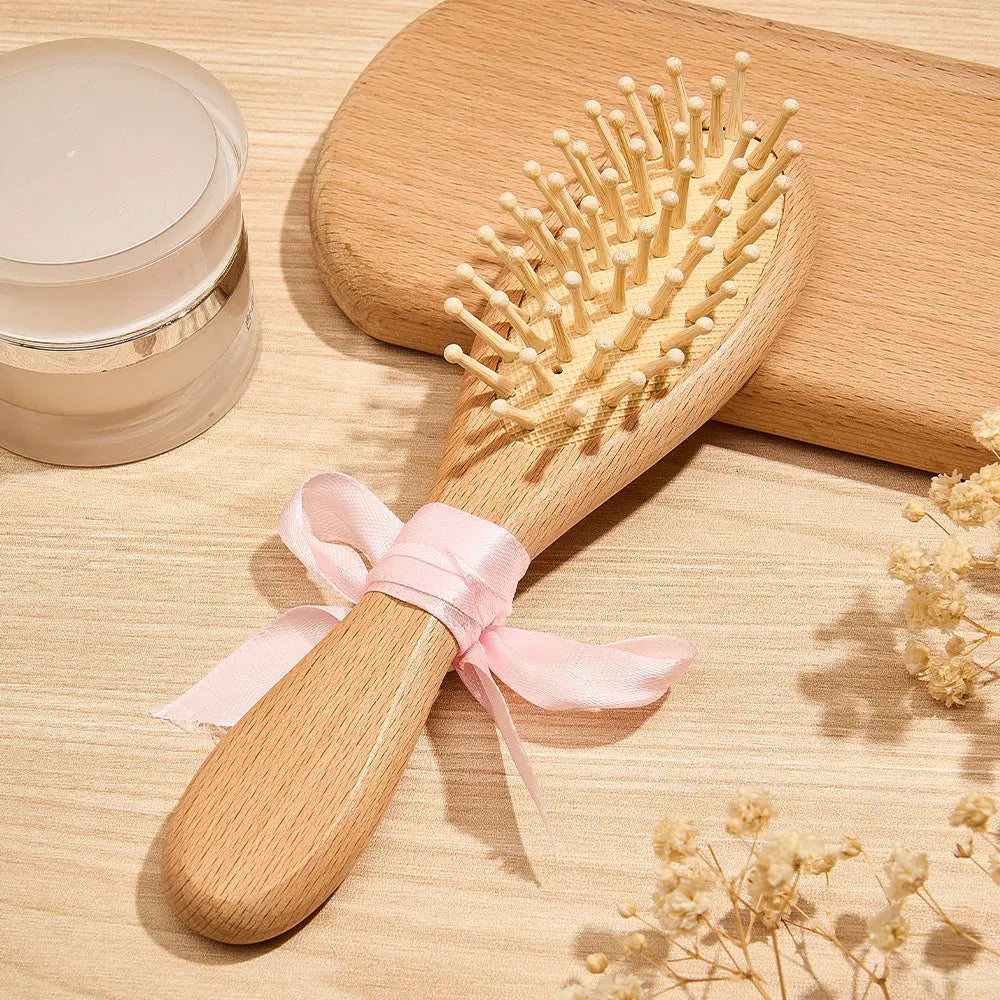Wooden hairbrush with a pink ribbon on a wooden surface with a jar and flowers.