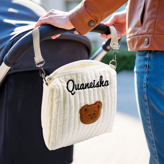 White quilted handbag with 'Quaneisha' and a bear patch held by a person with a stroller.