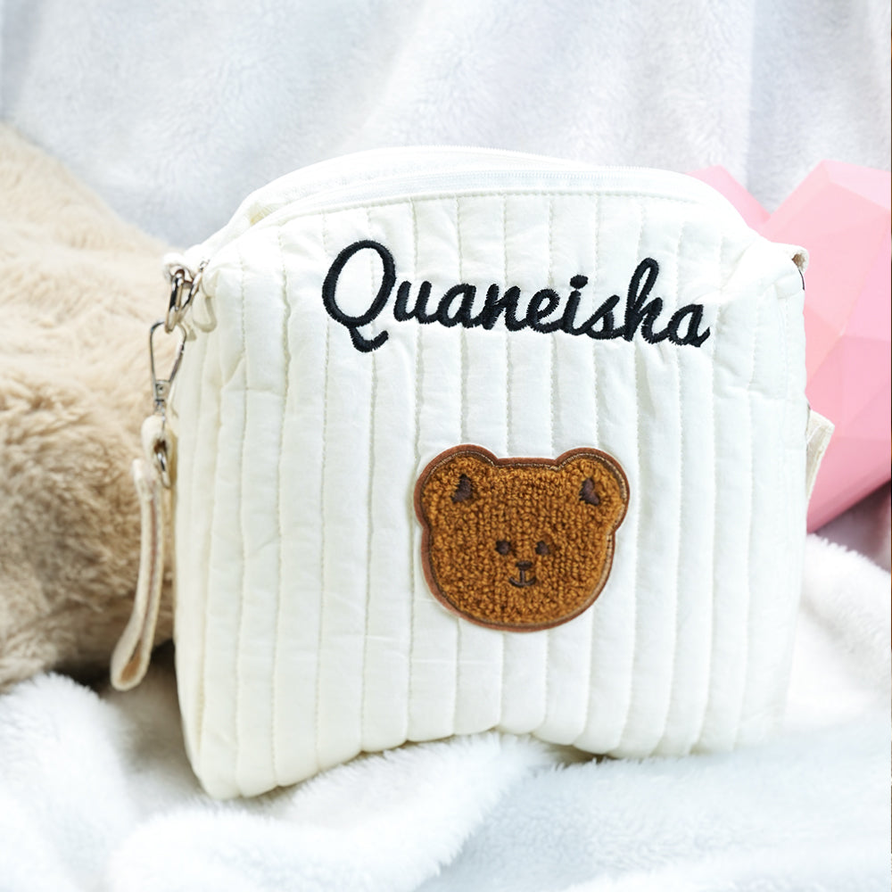 White textured pouch with 'Quaneisha' and a bear patch on a soft surface