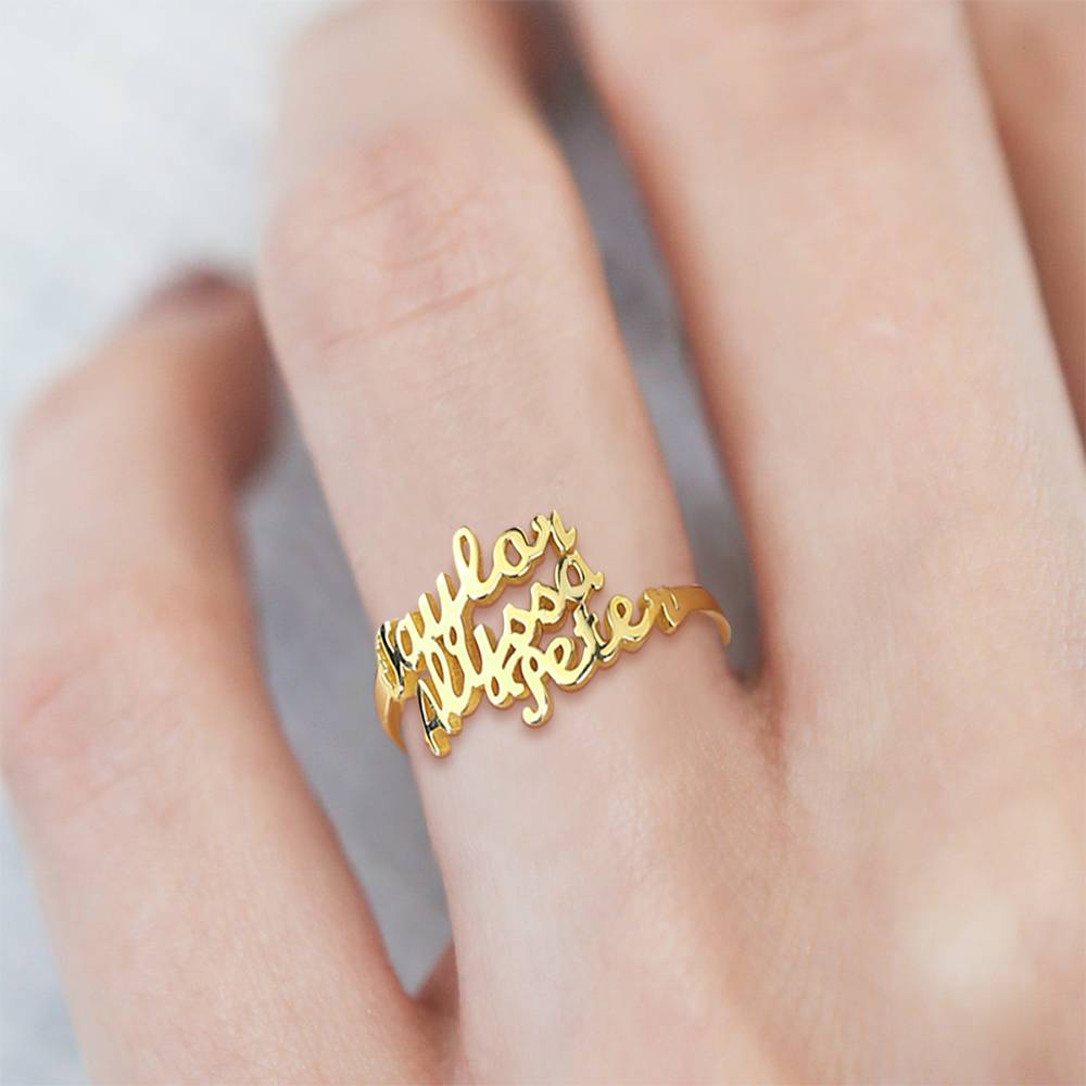 Gold ring with cursive text on a person's finger against a neutral background