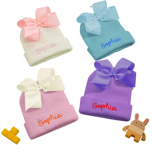 Four colorful baby hats with bows and embroidered names on a light green background