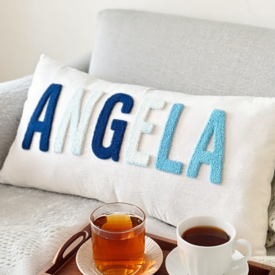 Decorative pillow with 'ANGELA' on a couch with tea and coffee.